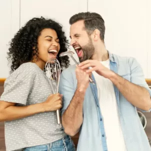 Couple happily singing in the kitchen, demonstrating the benefits of listening to music for your health and relationships