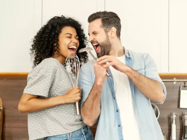 Couple happily singing in the kitchen, demonstrating the benefits of listening to music for your health and relationships