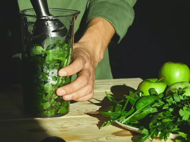 Man mixing a smoothie with various types of leafy greens to reap their health benefits