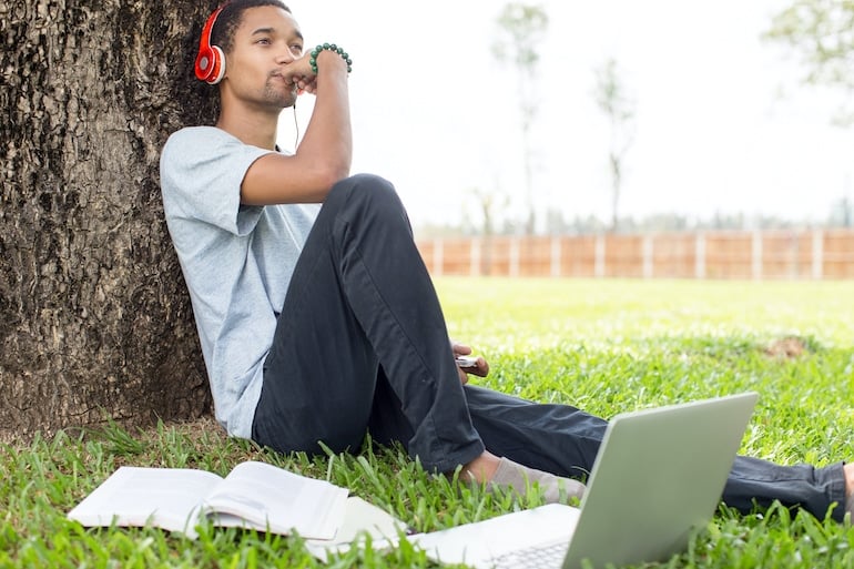 Man listening to music to benefit from productivity and creativity while working on laptop outdoors