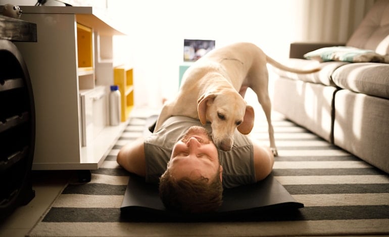 Dog licking its owner while he's on yoga mat, demonstrating the reduced stress health benefit of owning a pet