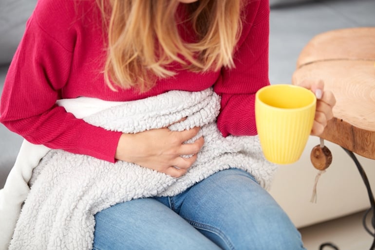 Woman drinking coffee and holding her stomach in discomfort from bloating