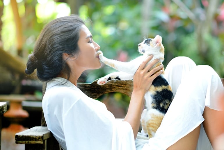 Woman outside kissing her cat's paw to show affection and health benefits of pets