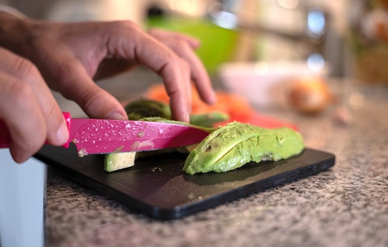 Woman cutting avocado to get healthy fats in her lunch