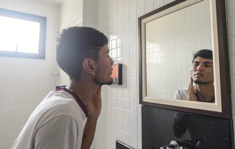 Young man investigating his acne in the mirror, which is a common symptom of hormonal imbalance