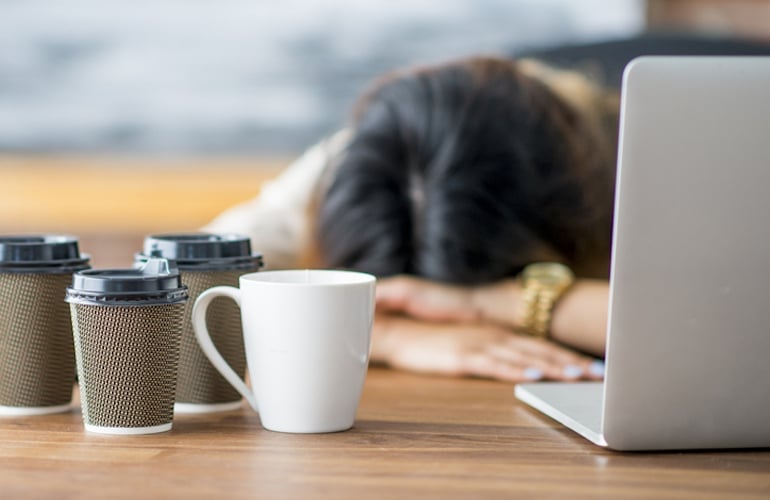 Tired woman crashing at her desk due to coffee slump and poor sleep