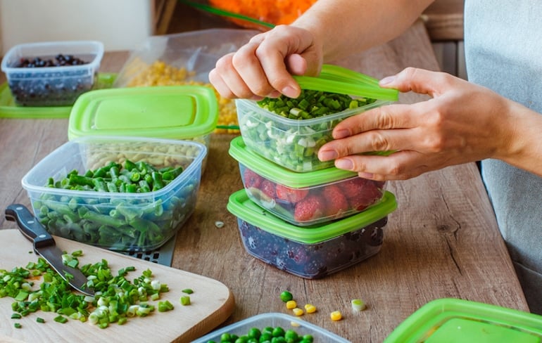 Woman prepping storage containers with produce as an easy sustainable eating tip