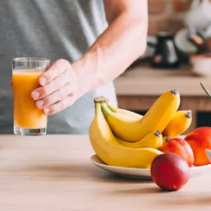Man in kitchen holding juice with bananas and apples to help reduce bloating