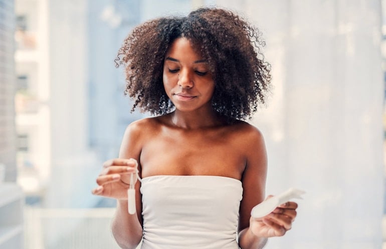 Woman holding tampon and pad in bathroom while on her period