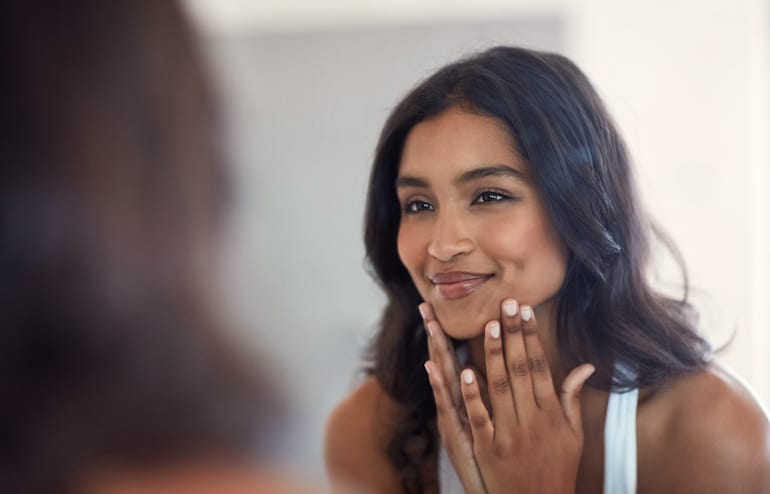 Woman looking at her bright, healthy skin in the mirror thanks to topical vitamin C