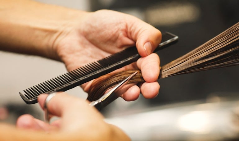 Hair stylist trimming a brunette's hair to help stop hair breakage and repair split ends