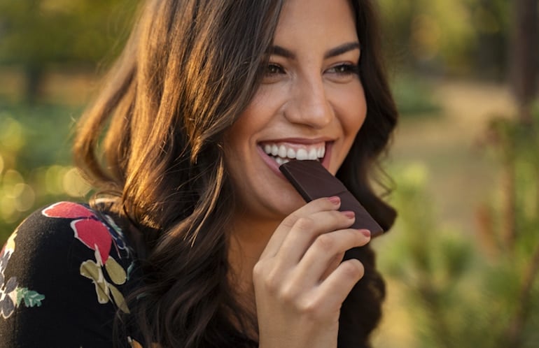 Happy woman eating a piece of dark chocolate, which has magnesium to help protect and boost mental health