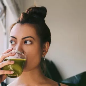 Pensive woman drinking green juice by the window, wondering if you can really boost your immune system through diet and lifestyle