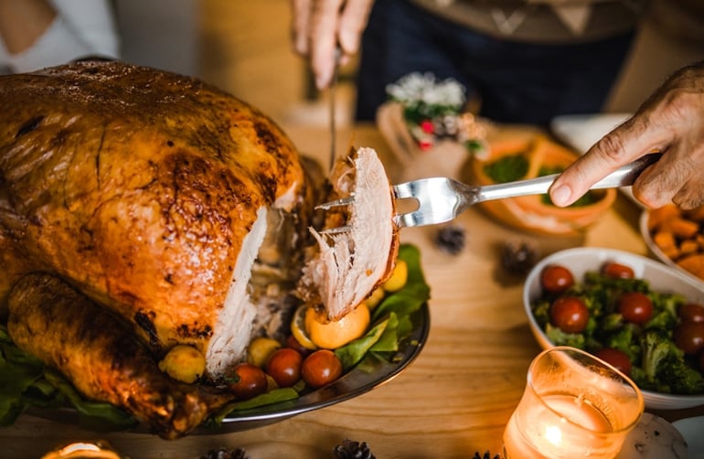 Man carving turkey on dinner table, which has tryptophan to promote mental and emotional well-being