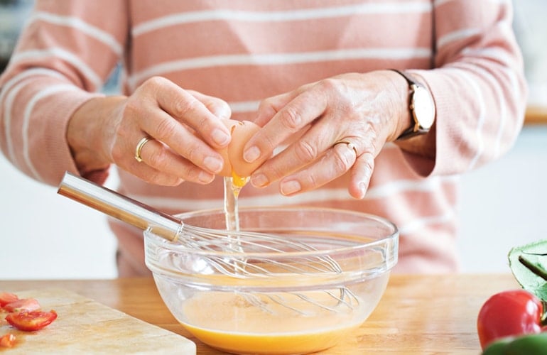 Woman in her 50s cracking eggs to get enough vitamin B12, following a dietitian's dietary requirements by age