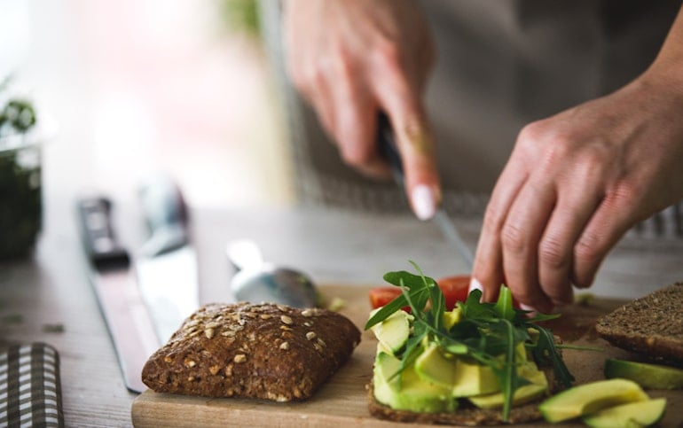 Person making a healthy vegetarian sandwich with avocado, tomato, and arugala to stay healthy via diet