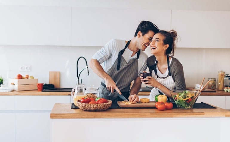 Happy couple cooking together in the kitchen, getting an oxytocin boost from physical intimacy