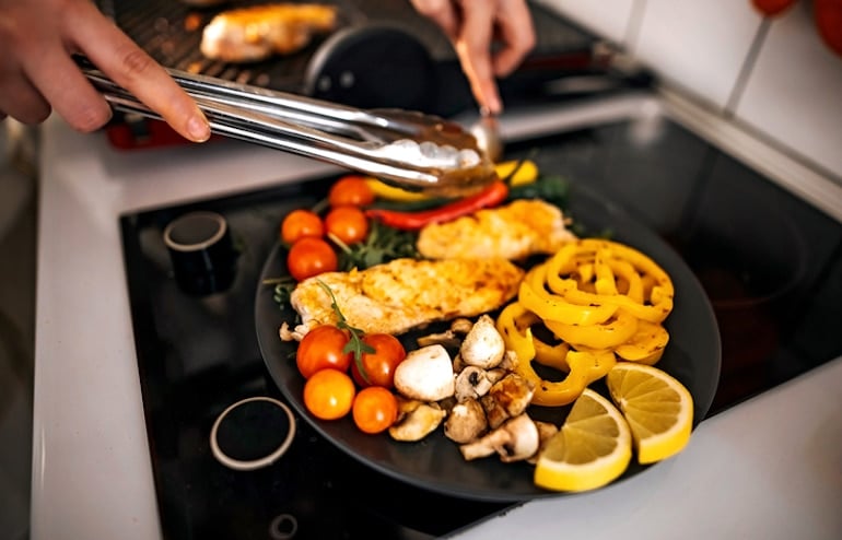 Woman in her 30s preparing a balanced meal with lean chicken and vegetables to maintain muscle mass as she ages