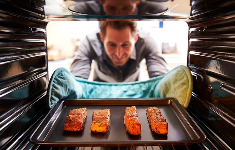 Man in his 40s taking salmon out of the oven to benefit from omega-3 intake