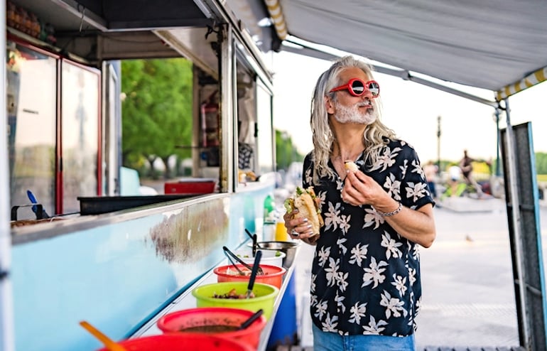 Man with long hair eating at a food stand