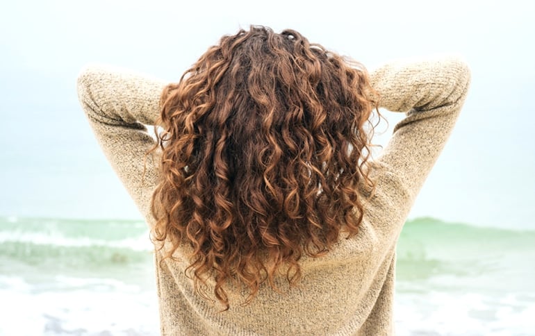 Woman with long curly hair tousling her hair at the beach after eating the best foods for hair growth