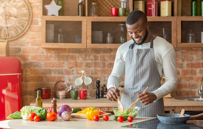 Man in his 20s tossing a colorful salad in the kitchen to get a variety of nutrients; concept of how your nutritional needs change over time