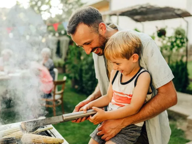 Father sharing grilling tips with his son at family barbecue