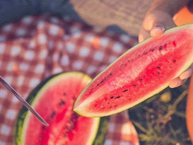 Man cutting into watermelon on a summer picnic blanket