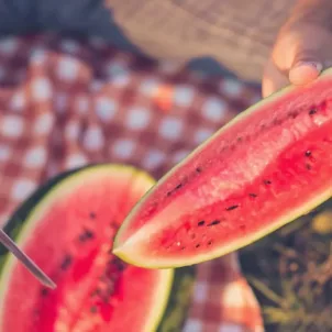 Man cutting into watermelon on a summer picnic blanket