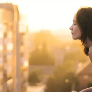 Woman peeking out of city balcony; anti-pollution skincare concept