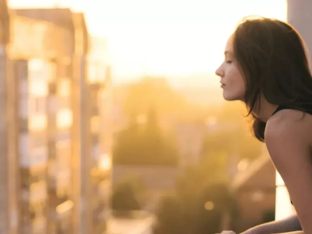 Woman peeking out of city balcony; anti-pollution skincare concept