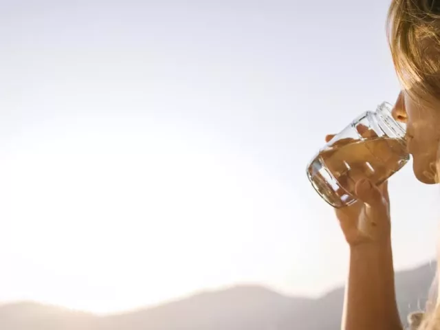 Woman taking supplements with water to address her summer beauty and wellness concerns