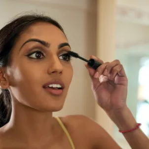 Indian woman applying mascara carefully in the mirror