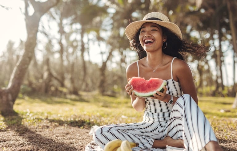 Young woman with hydrated, glowing skin eating watermelon at picnic