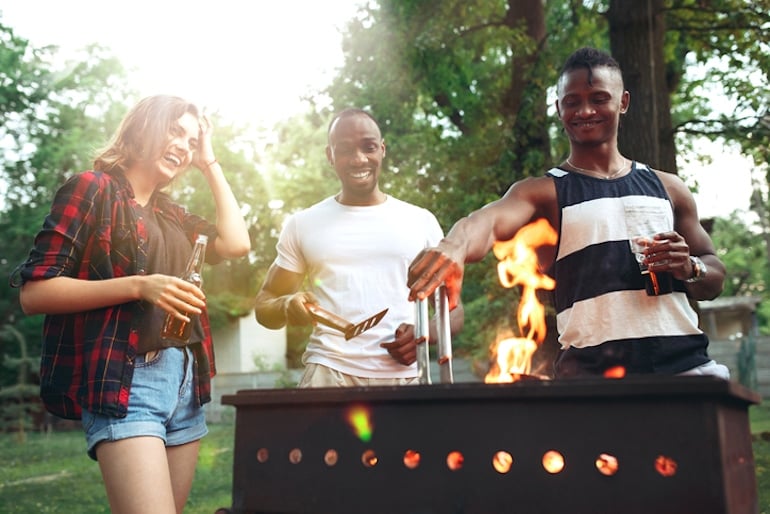 Friends drinking and grilling outdoors, moving food away from the flames