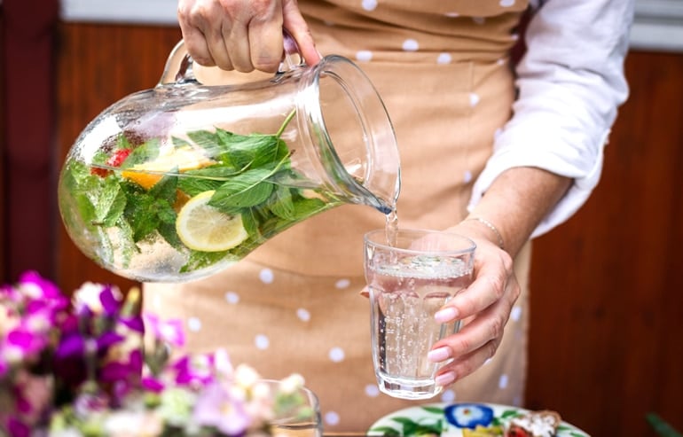 Woman pouring fruit-infused seltzer into glass at garden party