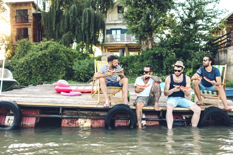 Male friends sitting by water eating watermelon for their nutritional benefits