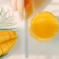 Woman holding straw next to mango and mango juice