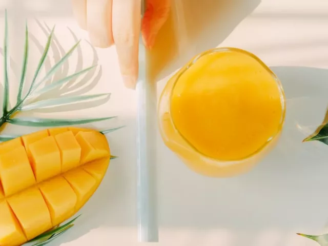 Woman holding straw next to mango and mango juice