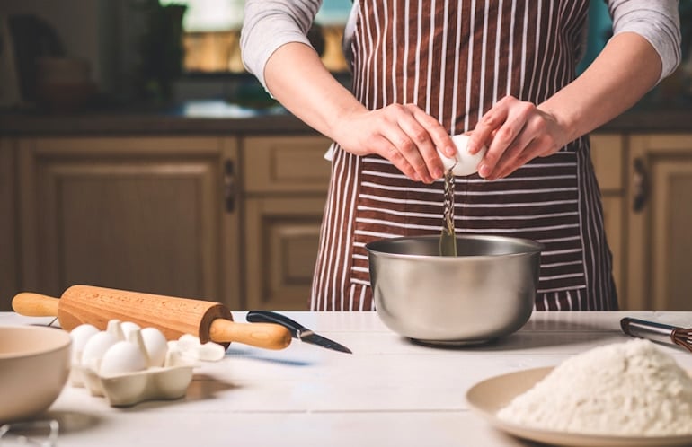 Woman breaking white organic eggs into bowl for baking