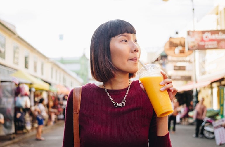 Woman with healthy skin drinking mango juice at outdoor market