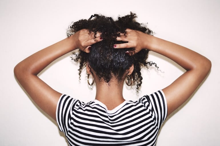 Back of woman's head with her curly hair in hands after taking the best vitamins for hair growth