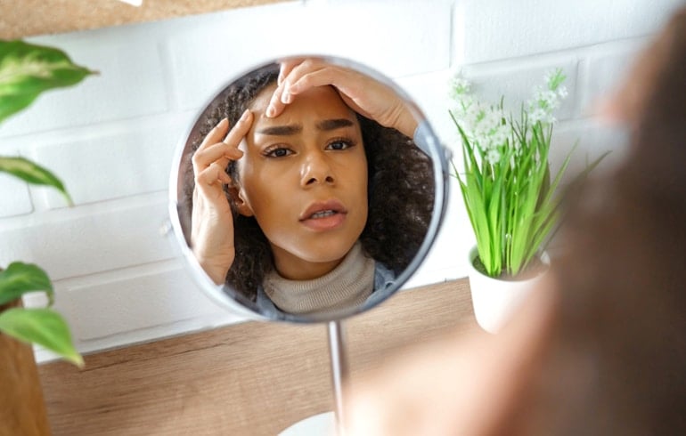 Woman looking at her breakout caused by acne in the mirror