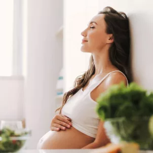 Pregnant woman with long hair sitting in the kitchen after taking a prenatal vitamin