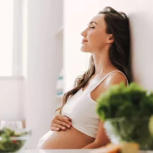 Pregnant woman with long hair sitting in the kitchen after taking a prenatal vitamin