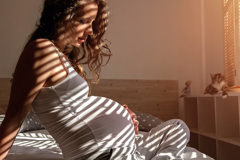 Pregnant woman with long curly hair touching belly on bed