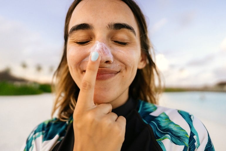 Woman on beach applying mineral SPF to her nose