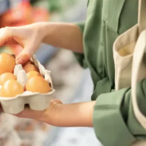 Woman at supermarket holding pasture-raised eggs, the best eggs to buy based on nutritional content and value