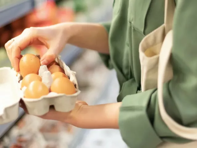 Woman at supermarket holding pasture-raised eggs, the best eggs to buy based on nutritional content and value