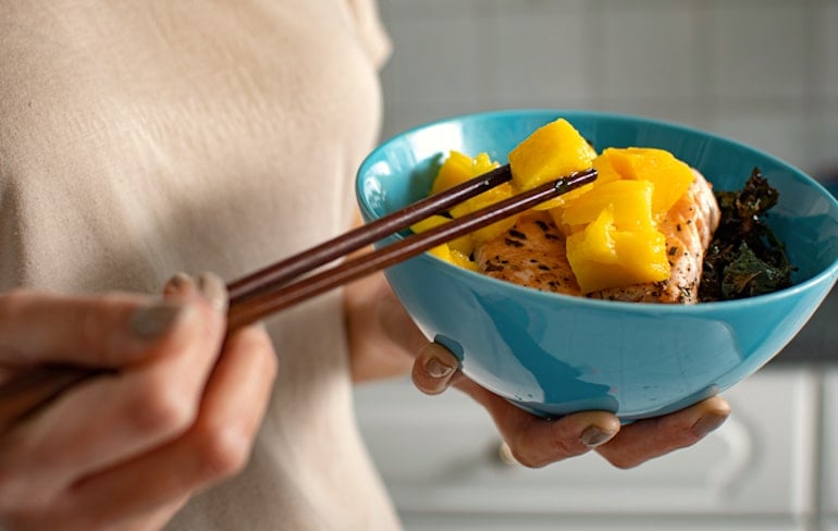 Woman eating salmon with mango for its nutritional benefits